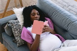 Picture: A pregnant woman is lying on a sofa and writing down notes.