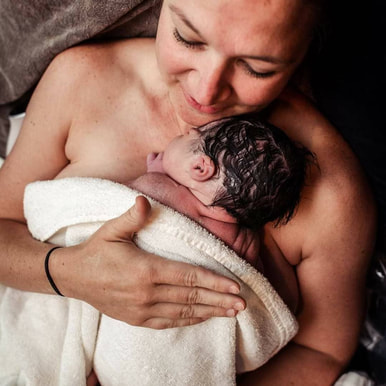 just born water birth dark haired baby held by smiling mom